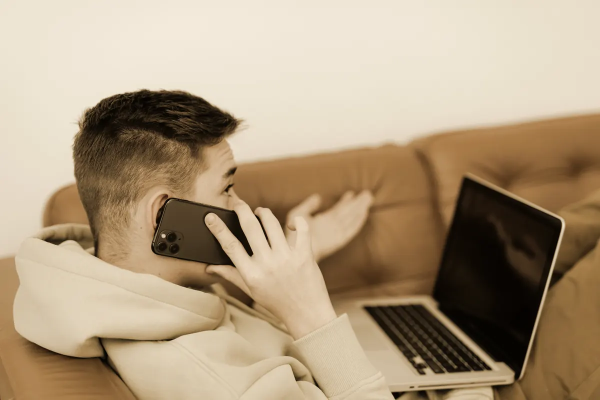 A young athlete on the phone at home, gesturing mid-conversation, a laptop open beside him