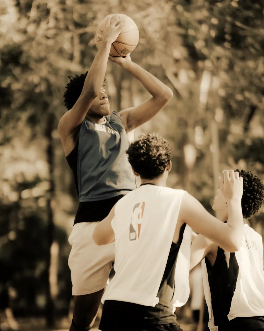 A young player rising for a jump shot over two defenders on an outdoor court