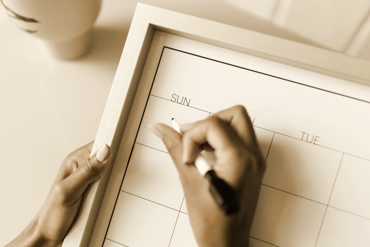 A blank weekly planner board being filled in with a marker