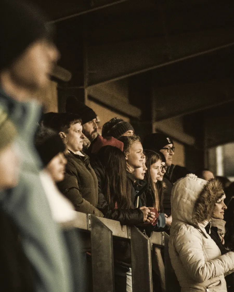 Parents and children watching a match from behind the barrier on a cold evening