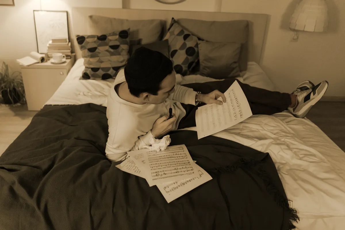 A young man alone on a bed going back over his own handwritten pages, pen in hand