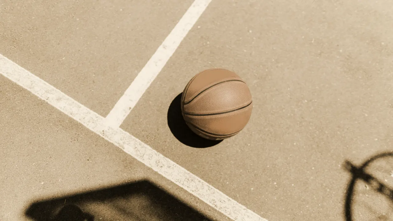 A single basketball left alone on an outdoor court beside the line