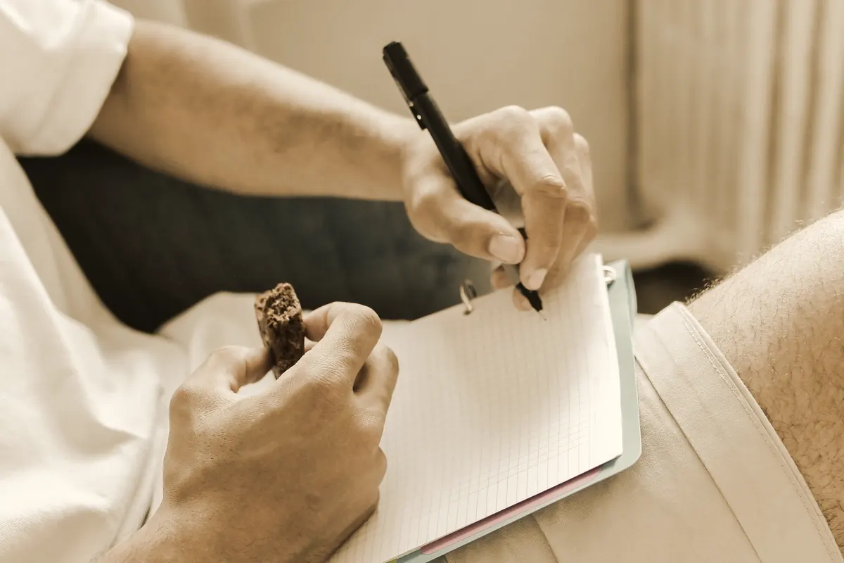 Close-up of hands writing in a ring-bound notebook resting on a lap