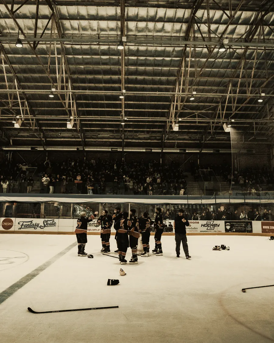 A hockey team gathered in a huddle at centre ice after a game, crowd in the stands behind
