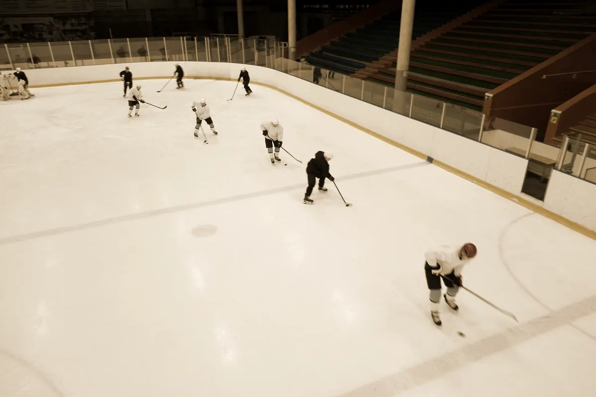 A hockey practice seen from above, players spread across the ice with one coach among them